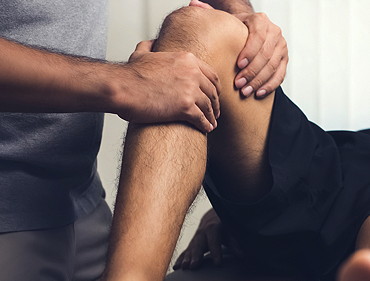 Hände des Physiotherapeuthen behandeln ein Knie