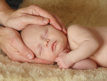 Hände von einem Erwachsenen halten schlafenden Babykopf